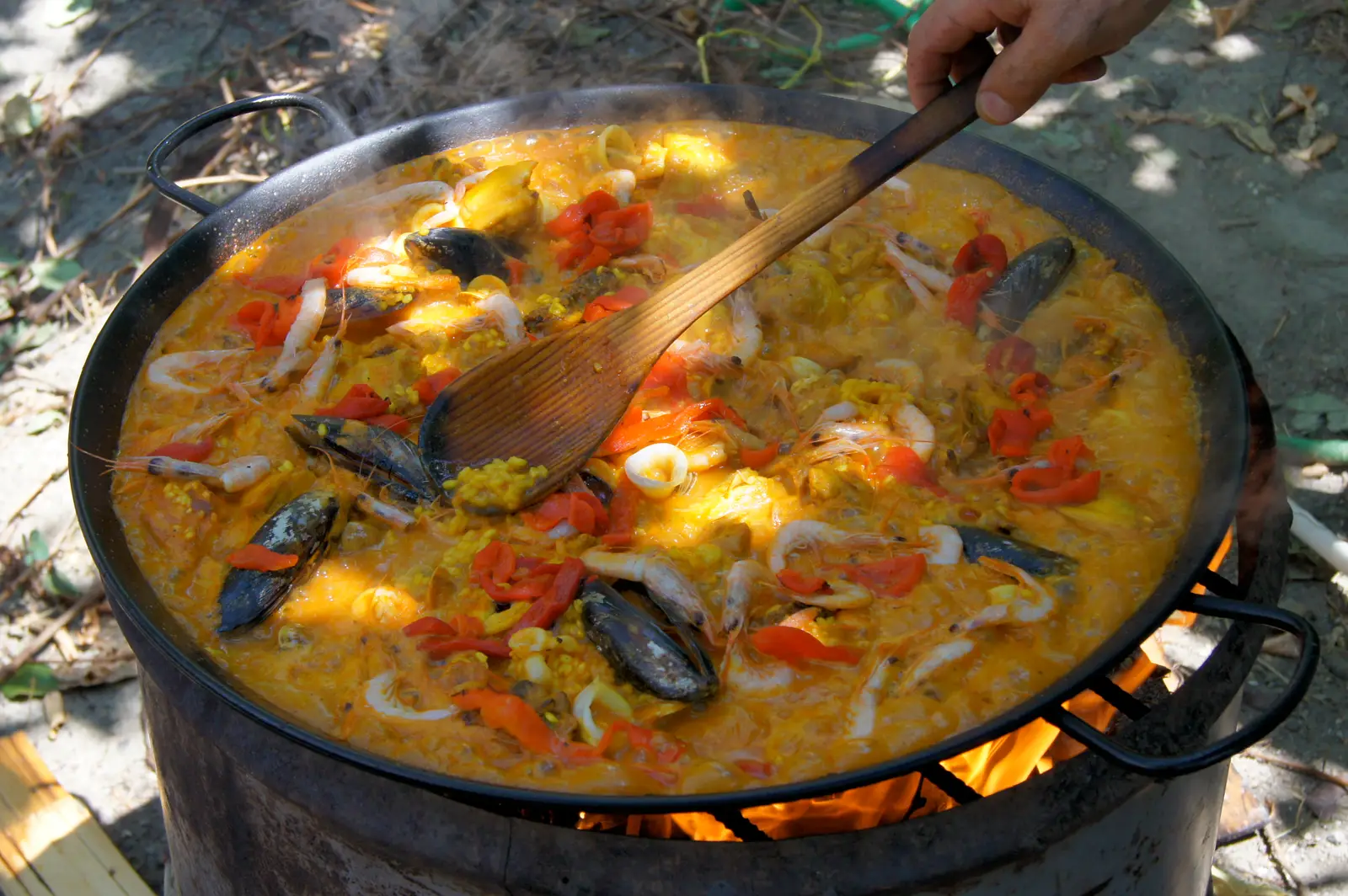 Una paella de marisco cocinándose al fuego mientras alguien la remueve con una cuchara de madera